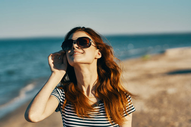 portrait of happy red-haired woman in nature on the beach near the sea and glasses on her face - Foto, Imagem