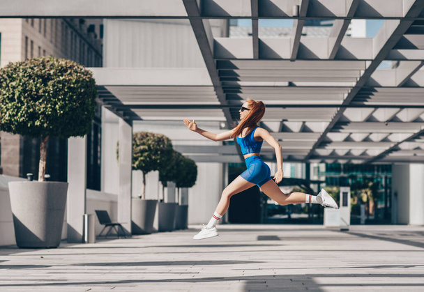 Athlete woman in sportswear doing sport exercises, running fast, jumping in Dubai on background of city buildings - Valokuva, kuva