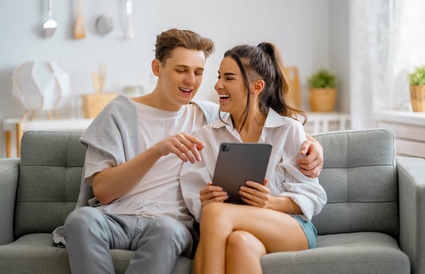 Young couple is using tablet pc. Woman and man having fun staying at home. - Foto, afbeelding