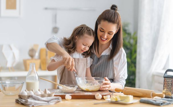 Happy loving family are preparing bakery together. Mother and child daughter girl are cooking cookies and having fun in the kitchen. Homemade food and little helper.  - Zdjęcie, obraz