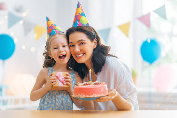 The kid is blowing out the candles on the cake. Mother and daughter are celebrating birthday. - 写真・画像