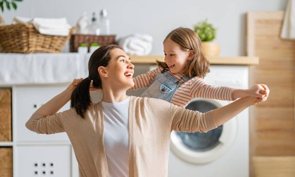 Beautiful young woman and child girl little helper are having fun and smiling while doing laundry at home. - Foto, Bild