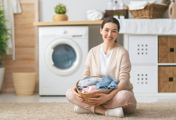 Beautiful young woman is smiling while doing laundry at home. - Foto, Imagen