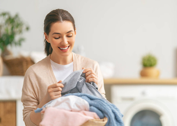 Beautiful young woman is smiling while doing laundry at home. - Photo, image