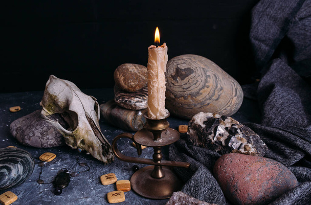 Παλιό κρανίο σκύλου, αναμμένο κερί, ξύλινοι ρούνοι και πέτρες στο τραπέζι των μαγισσών. - Φωτογραφία, εικόνα