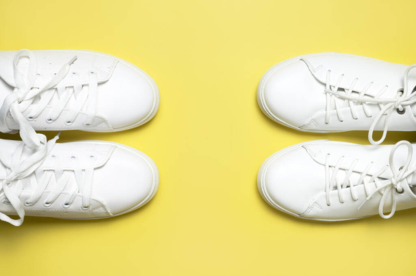 White sneakers on yellow background top view flat lay. Stylish youth women's leather sneakers, sports shoes, genuine leather footwear. Minimalistic shoe store advertising fashion style Shoe background. - Photo, Image