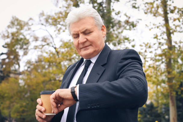 Ανώτερος επιχειρηματίας κοιτάζοντας ρολόι χειρός στο πάρκο - Φωτογραφία, εικόνα