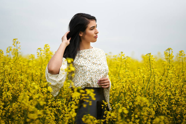 Beautiful brunette hispanic young woman in a blooming canola field - Fotó, kép