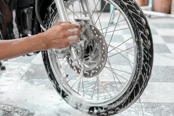 Close-up da mão de um homem lavando as rodas de uma moto com esponjas e bolhas. - Foto, Imagem