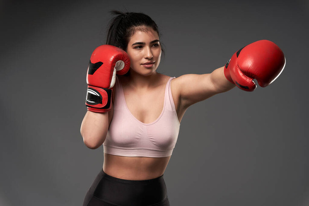 Plus size young hispanic woman boxer in red boxing gloves training on gray background - Zdjęcie, obraz