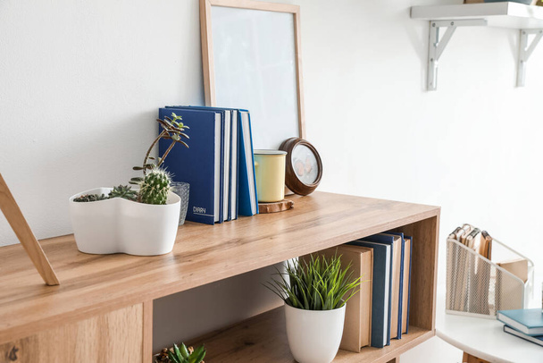 Одиниця полиці з книгами та рослинами біля світлої стіни
 - Фото, зображення