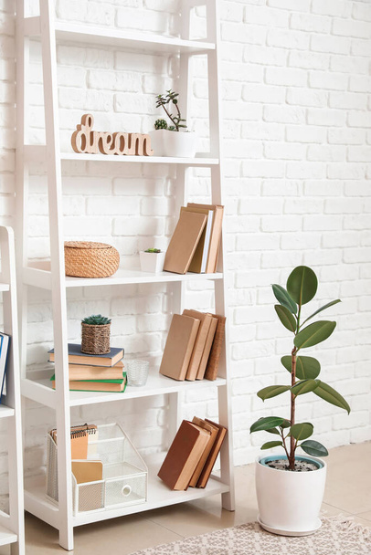 Shelf unit with books and decor near light brick wall - Zdjęcie, obraz