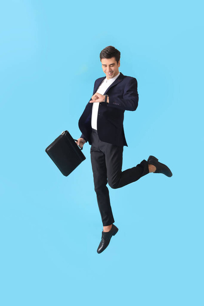 Jumping man with briefcase and wristwatch on color background - Foto, Bild