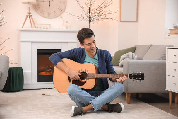 Красивый человек играет на гитаре возле камина дома - Фото, изображение