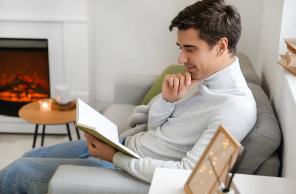Handsome man reading book near fireplace at home - Foto, Imagen