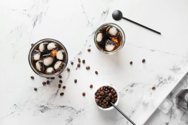 Glasses of tasty cold brew and coffee beans on light background - Foto, imagen