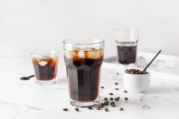 Glasses of tasty cold brew and coffee beans on light background - Foto, imagen