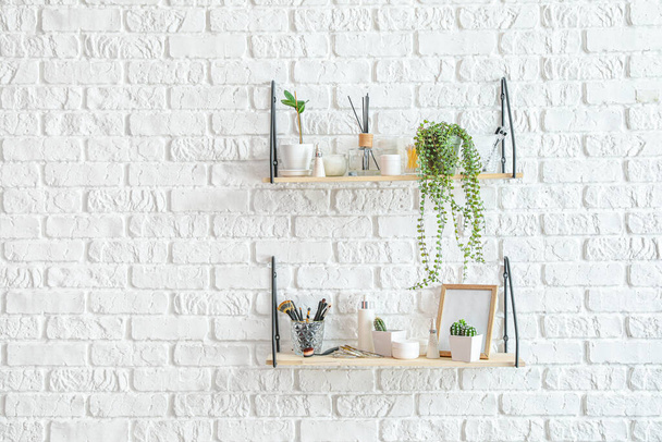 Shelves with houseplants and decor hanging on brick wall - Фото, изображение