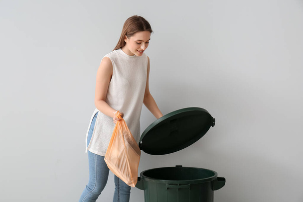 Young woman putting garbage in trash bin on light background - Фото, изображение