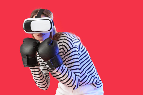 Young woman in boxing gloves and with virtual reality glasses on color background - Foto, afbeelding