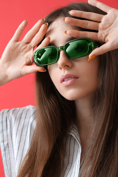 Bella giovane donna con eleganti occhiali da sole su sfondo di colore - Foto, immagini