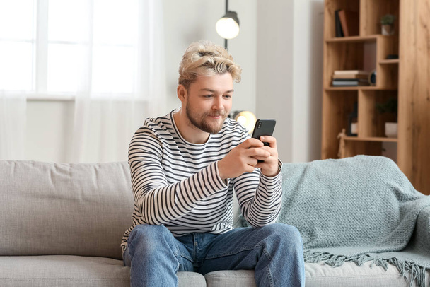 Fiatal férfi mobiltelefonnal otthon - Fotó, kép