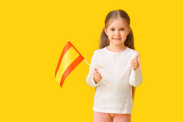Маленька дівчинка з прапором Іспанії показує пальцем вгору на кольоровому фоні - Фото, зображення