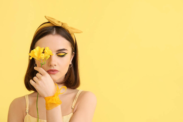 Stylish young woman with flower on yellow background - Фото, изображение