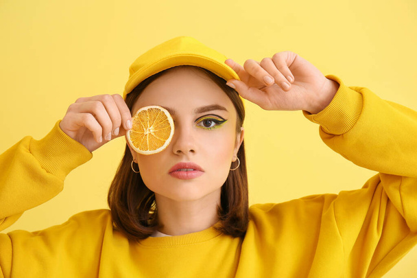 Stylish young woman with orange slice on yellow background - Photo, image