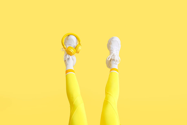 Legs of stylish young woman with headphones on yellow background - Foto, imagen