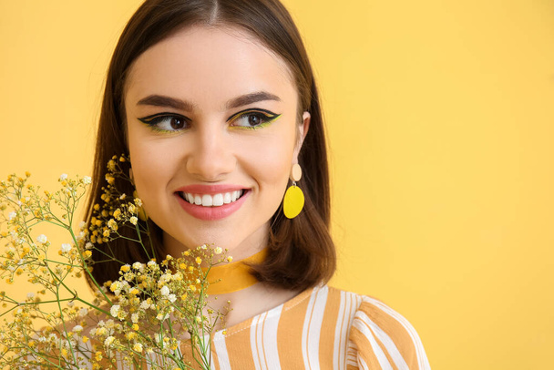 黄色の背景に花を持つスタイリッシュな若い女性 - 写真・画像