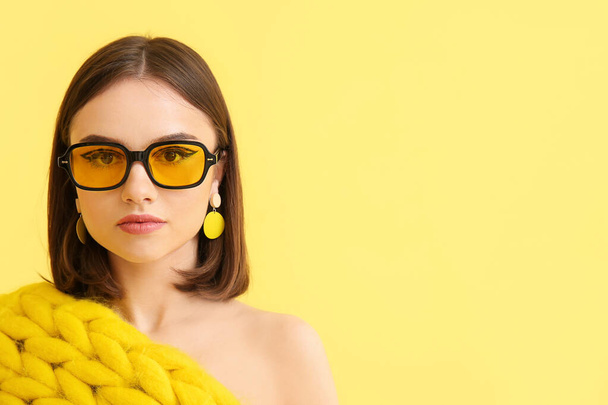Stylish young woman with knitted plaid and sunglasses on yellow background - Foto, imagen