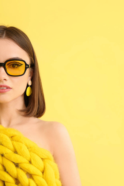 Stílusos fiatal nő kötött kockás és napszemüveg sárga alapon - Fotó, kép