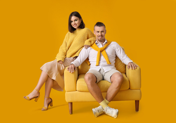 Stylish young couple with armchair on yellow background - Photo, Image