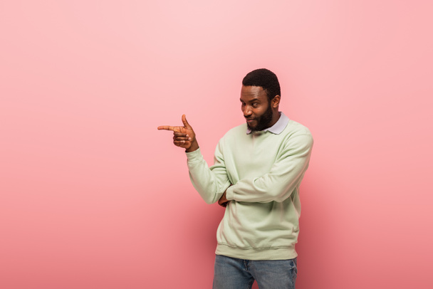 Smiling african american man pointing at pink background  - Zdjęcie, obraz