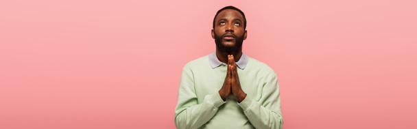 Αφροαμερικάνος με χέρια που προσεύχονται κοιτώντας απομονωμένα στο ροζ, πανό  - Φωτογραφία, εικόνα