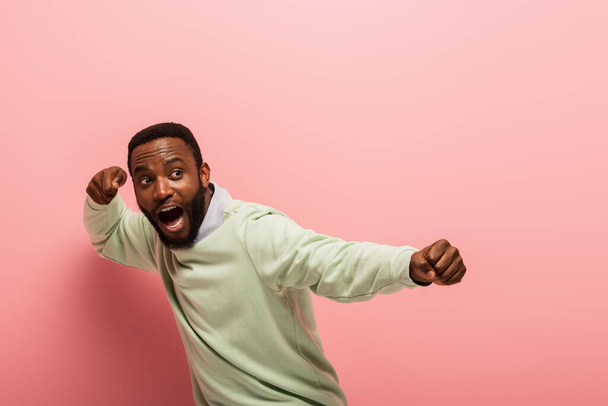 Screaming african american man with hands in fists on pink background  - Zdjęcie, obraz