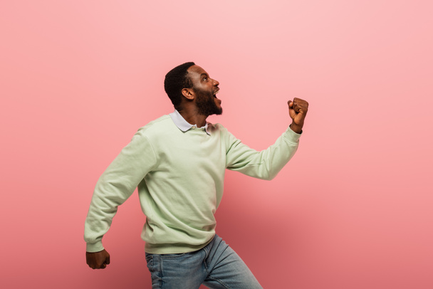 Vista lateral del hombre afroamericano emocionado mostrando sí gesto sobre fondo rosa  - Foto, imagen