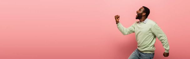 Вид сбоку изумленного африканского мужчины, показывающего жест Фабрегаса на розовом фоне, баннер  - Фото, изображение