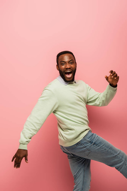 Cheerful african american man looking at camera while walking on pink background  - Foto, Bild