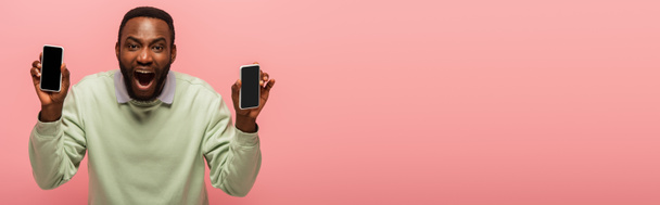Excited african american man with smartphones isolated on pink, banner  - Foto, afbeelding