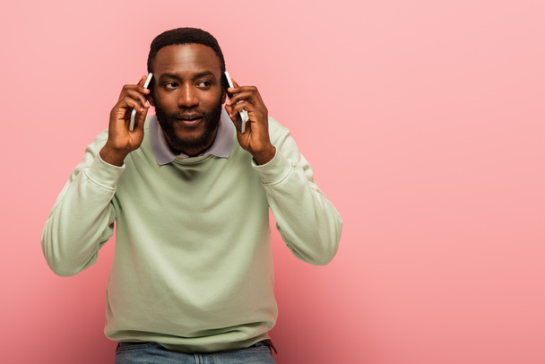 Young african american man talking on mobile phones on pink background  - Photo, Image