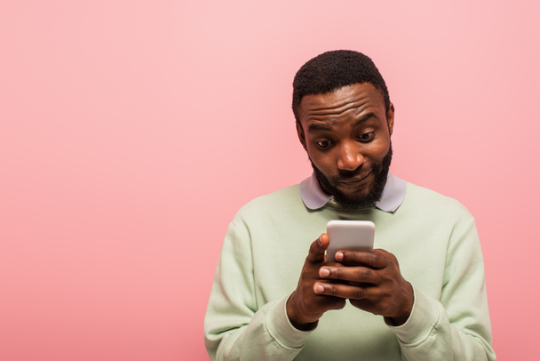 Hombre afroamericano mensajes de texto en el teléfono inteligente aislado en rosa  - Foto, Imagen