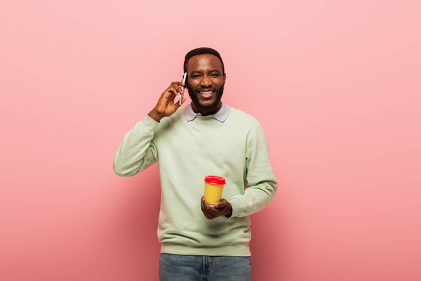 Africano americano com café para ir falar no celular em fundo rosa  - Foto, Imagem