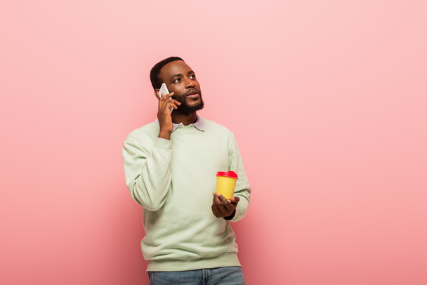 Afrikanischer Mann telefoniert mit Handy und hält Kaffee, um auf rosa Hintergrund zu gehen  - Foto, Bild