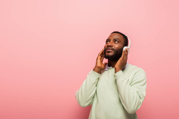 Joven afroamericano escuchando música en auriculares sobre fondo rosa  - Foto, imagen