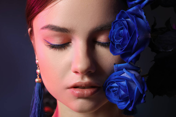 Beautiful young woman with blue roses on dark background, closeup - 写真・画像