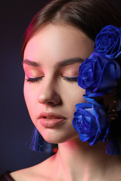 Piękna młoda kobieta z niebieskimi różami na ciemnym tle - Zdjęcie, obraz