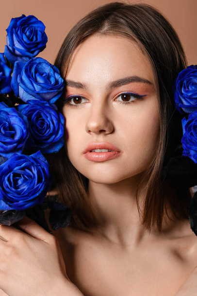 Όμορφη νεαρή γυναίκα με μπλε τριαντάφυλλα στο φόντο χρώμα - Φωτογραφία, εικόνα