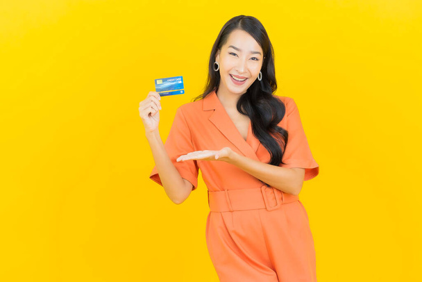 Muotokuva kaunis nuori aasialainen nainen hymyillä luottokortilla keltaisella värillä taustalla - Valokuva, kuva
